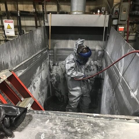 Circle-Prosco technician in protective gear cleaning out a pretreatment tank